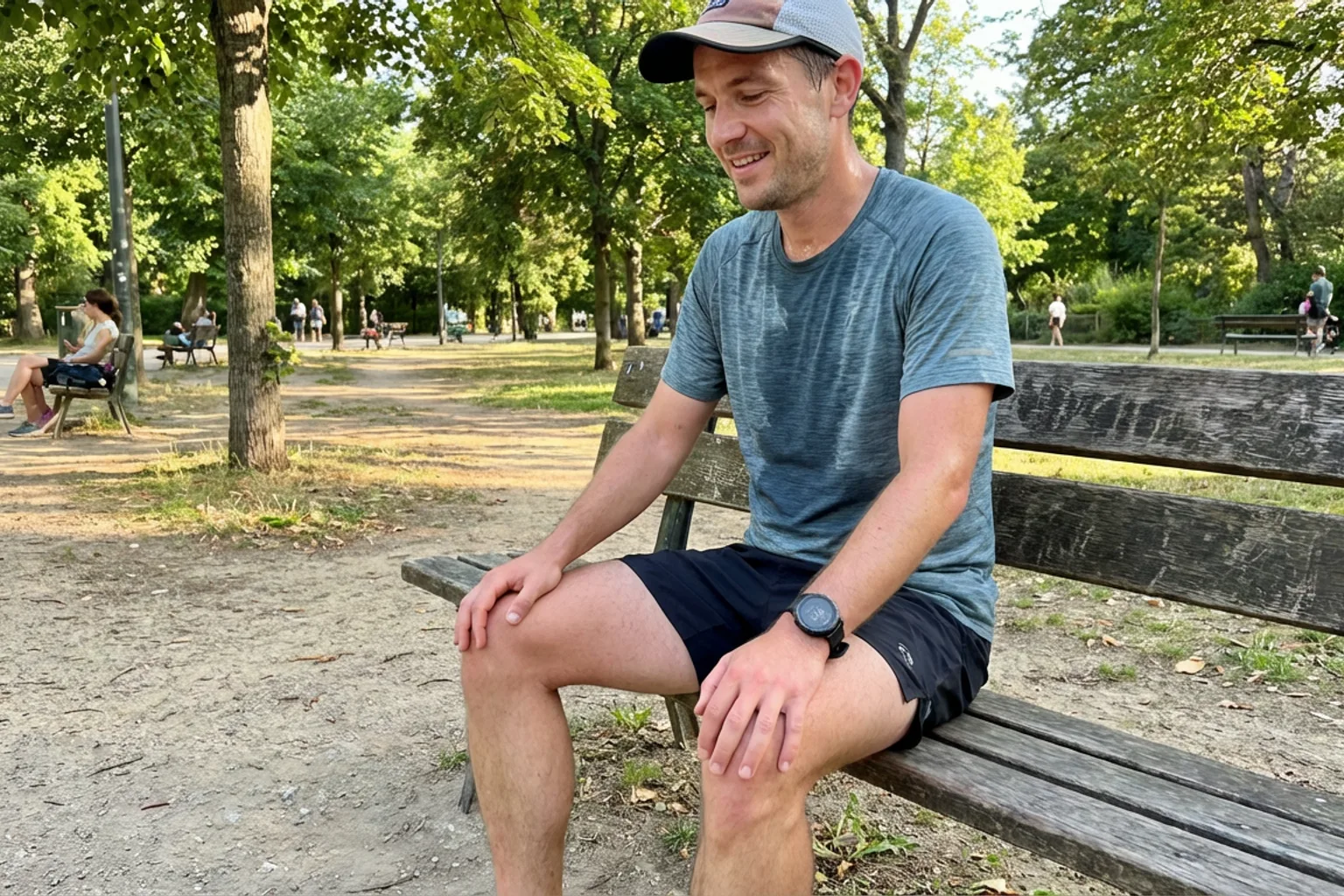 Candid iPhone photo of a fit male runner sitting on a park bench after a run, slightly sweaty, hands on knees, looking r