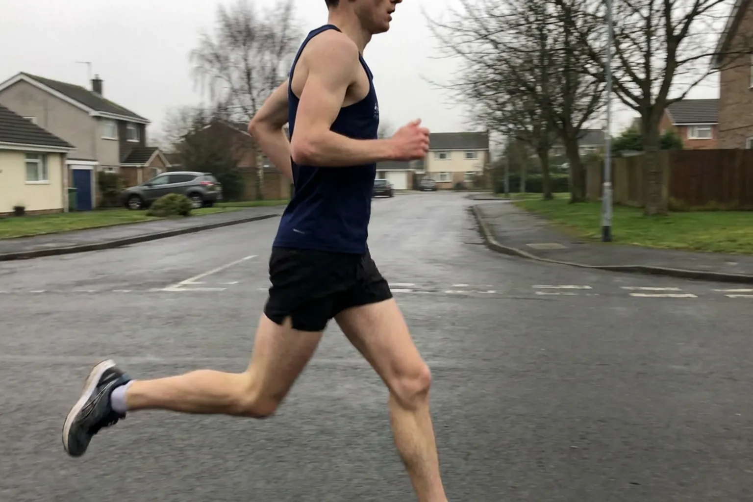 Candid iPhone photo of a lean athletic runner on a quiet road doing a short stride acceleration, slightly off-centre fra