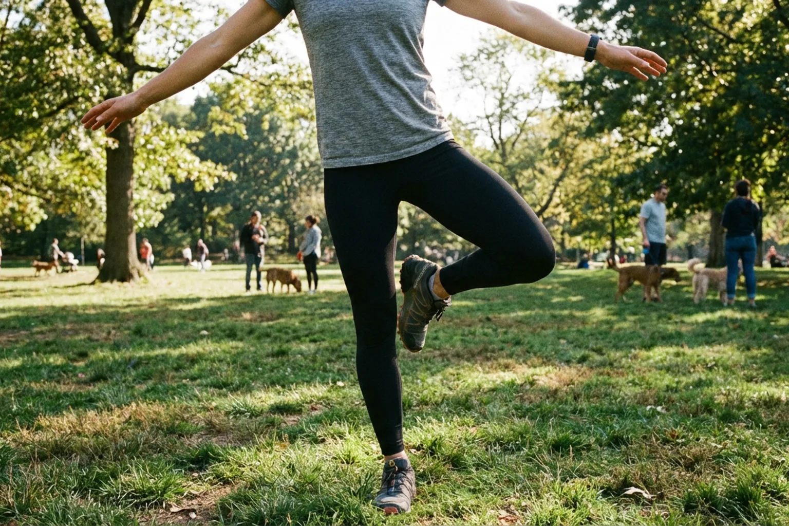 Candid iPhone photo of an athletic woman balancing on one leg on a grass surface outdoors, arms slightly out for balance