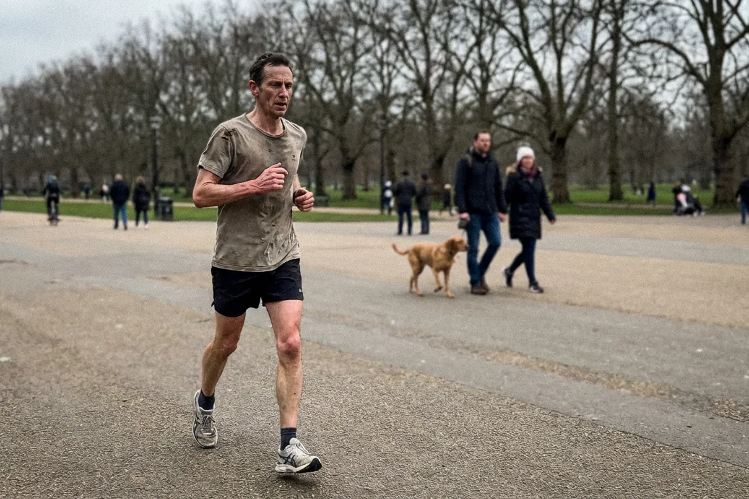 Candid iPhone photo of a lean male runner on a flat park path, mid-stride, slightly off-centre framing, overcast natural