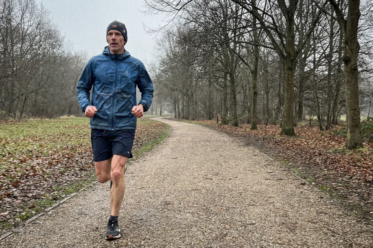 Candid iPhone photo of a lean male runner in his mid-40s mid-stride on a quiet park path, overcast morning light, wearin